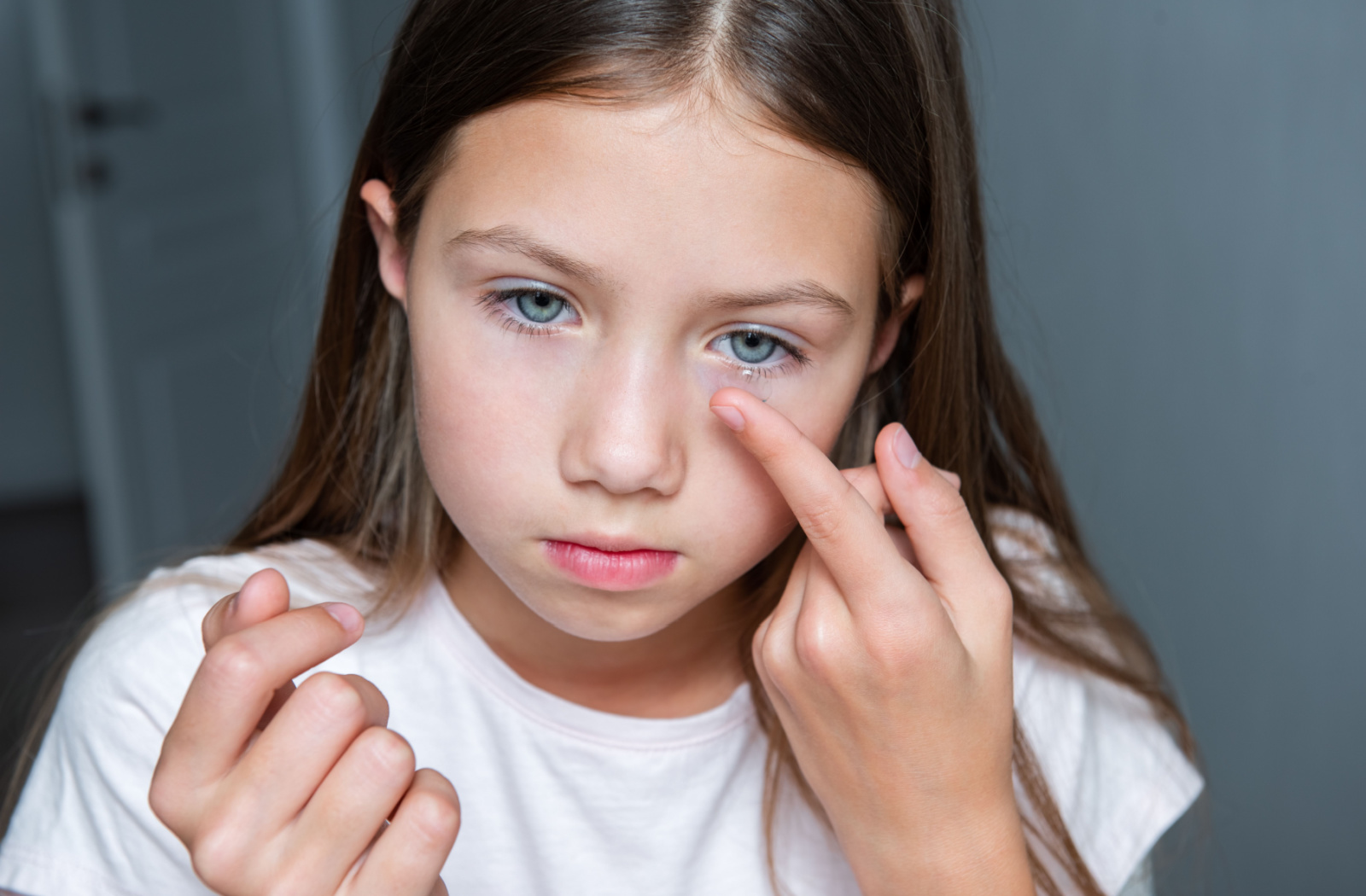 A young girl in a white shirt putting an ortho-k lens in her left eye.