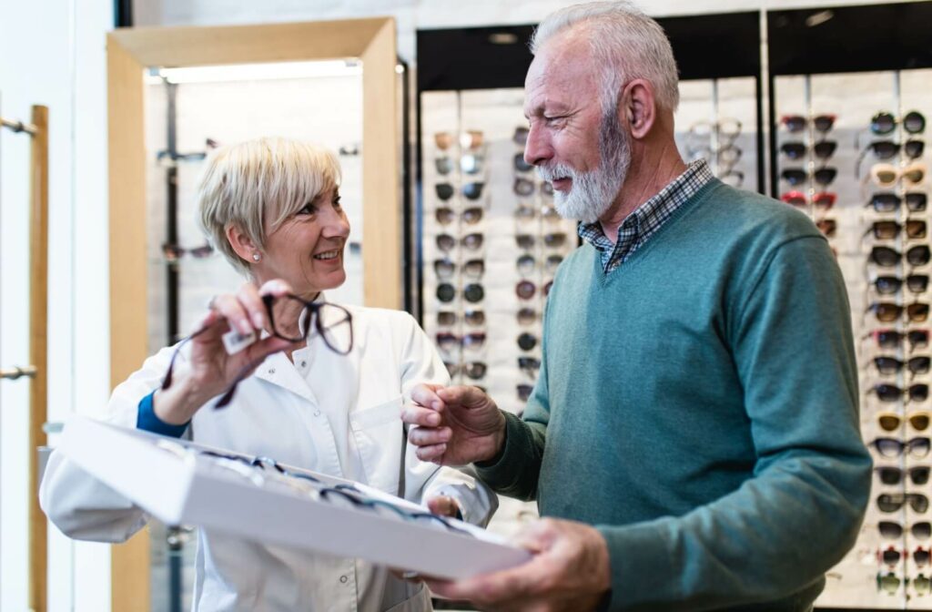 An optometrist picks up a pair of progressive glasses from a tray and explains their benefits to the patient.