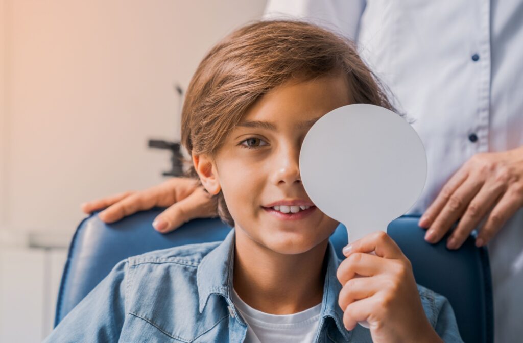 Young boy at optometrist covering eye with occluder during eye exam.